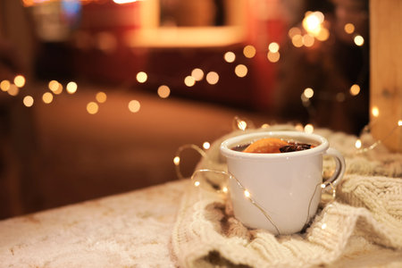 Cup of hot mulled wine and garland on table against blurred background. Space for textの写真素材