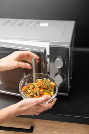 Young woman using microwave oven on table in kitchenの写真素材