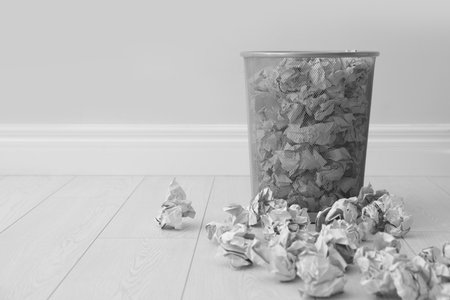 Metal bin and crumpled paper against light wall, space for textの写真素材