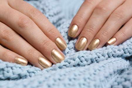 Woman with manicure golden holding knitted fabric, closeup. Nail polish trendsの写真素材