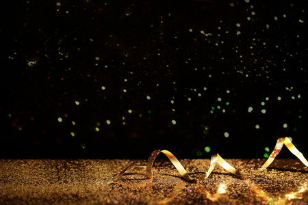 Golden glitter and streamer against black background. Space for textの写真素材