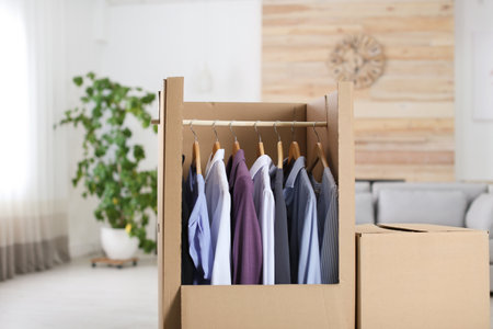 Cardboard wardrobe box with clothes on hangers in living roomの写真素材
