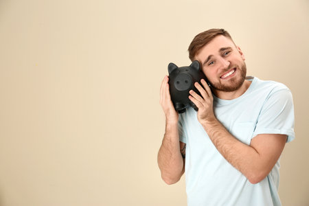 Happy young man with piggy bank and space for text on color background. money savingの写真素材