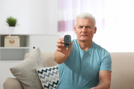 Senior man holding digital glucometer at home. Diabetes controlの写真素材