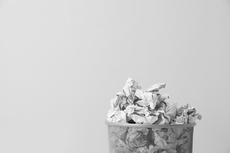 Metal bin with crumpled paper against light background, space for textの写真素材