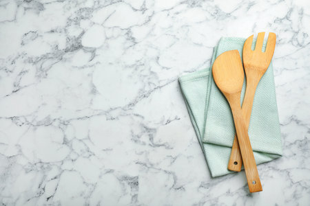 Wooden spatula, fork and napkin on marble background, top view with space for textの写真素材