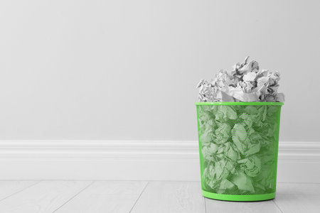 Metal bin and crumpled paper against light wall, space for textの写真素材