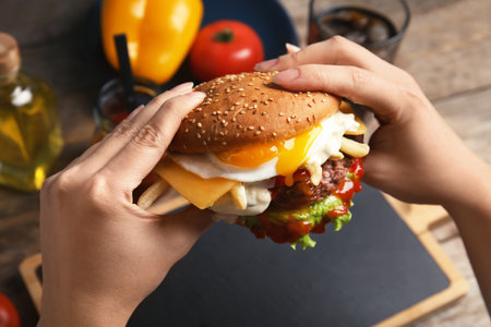 Woman holding tasty burger with fried egg over table, closeupの写真素材