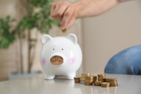 Man putting coin into piggy bank at table indoors, selective focus. money savingの写真素材