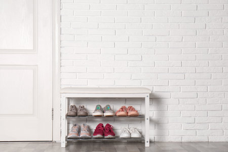 Shoe storage bench with different sneakers near brick wall, space for text