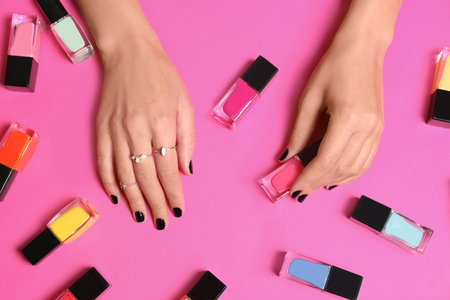 Woman with black manicure and nail polish bottles on color background, top viewの写真素材