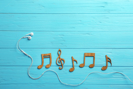 Earphones and music notes on wooden background, flat lay. Space for textの写真素材