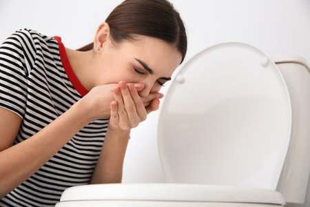 Young woman suffering from nausea at toilet bowl indoorsの写真素材
