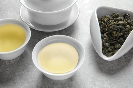 Cups of Tie Guan Yin oolong and chahe with tea leaves on gray tableの写真素材