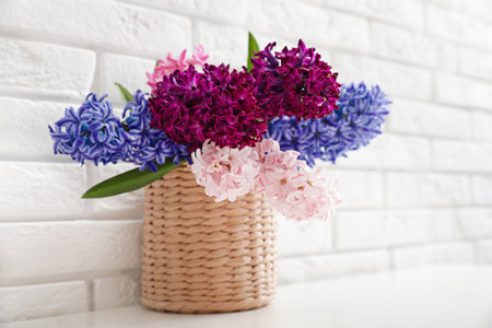 Beautiful hyacinths in wicker pot on table against brick wall, space for text. spring flowersの写真素材
