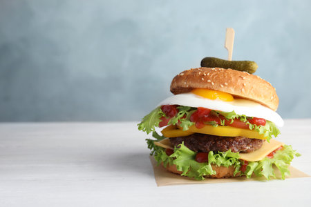 Tasty burger with fried egg on table against color background, space for textの写真素材