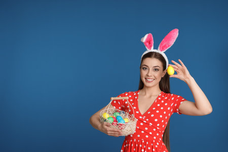 Beautiful woman in bunny ears headband with Easter eggs on color background, space for textの写真素材