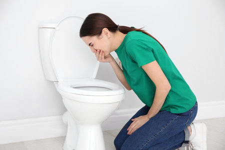 Young woman suffering from nausea over toilet bowl indoorsの写真素材