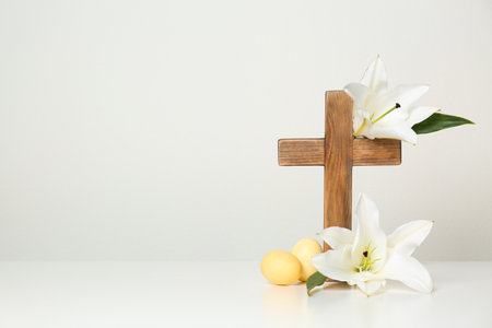 Wooden cross, Easter eggs and blossom lilies on table against light background, space for textの写真素材