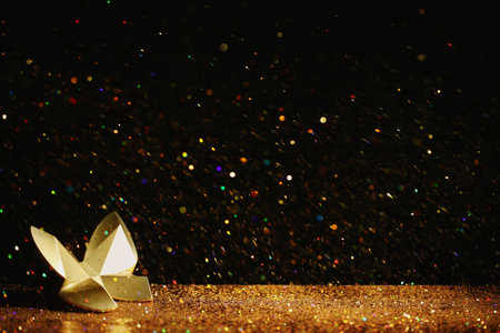 Golden glitter and decorative butterfly against black background. Space for textの写真素材