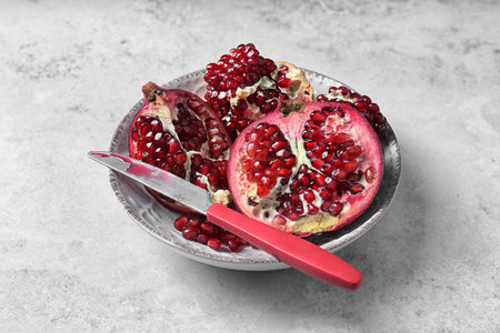 Plate with ripe pomegranates and knife on gray background
