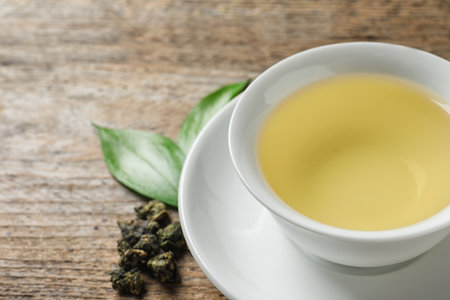 Cup of Tie Guan Yin oolong and tea leaves on wooden table, closeup. Space for textの写真素材