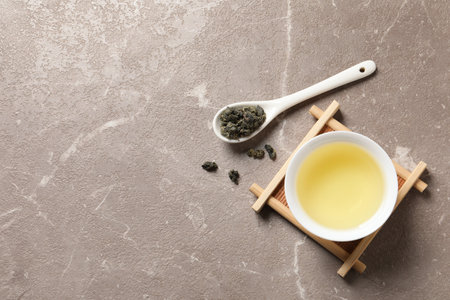 Cup of Tie Guan Yin oolong and spoon with tea leaves on table, top view. Space for text