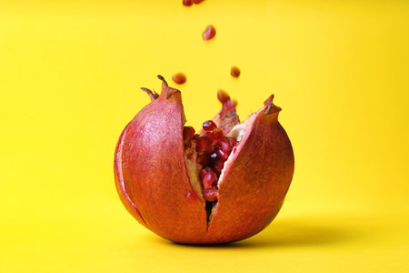 Delicious red ripe pomegranate and falling seeds on color backgroundの写真素材