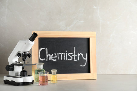 Laboratory glassware, microscope and board with word CHEMISTRY on table against gray background. Space for textの写真素材