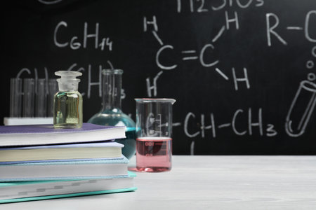 Laboratory glassware and school supplies on table against blackboard with chemical formulasの写真素材