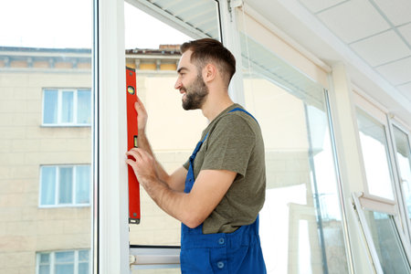 Construction worker using bubble level while installing window indoors