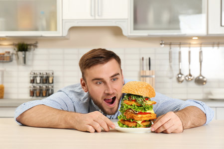 Young hungry man and huge burger on tableの写真素材