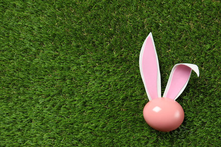 Flat lay composition of funny Easter bunny ears and dyed egg on green grass, space for textの写真素材