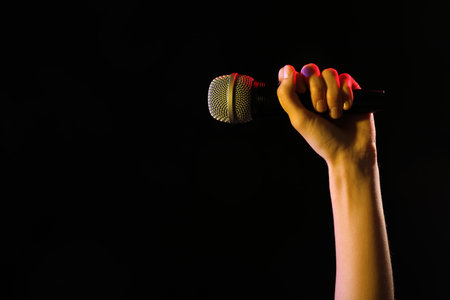 Woman holding microphone on black background, closeup. Space for textの写真素材