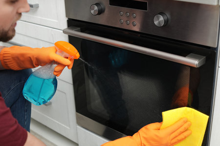 Young man cleaning oven with rag and detergent in kitchen, closeupの写真素材