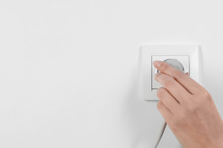 Woman putting plug into power socket on white background, closeup. Electrician's equipmentの写真素材