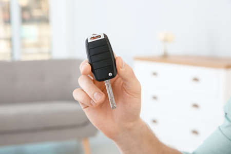 Young man with new car key in dealership, closeup