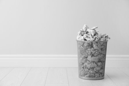 Metal bin and crumpled paper against light wall, space for textの写真素材