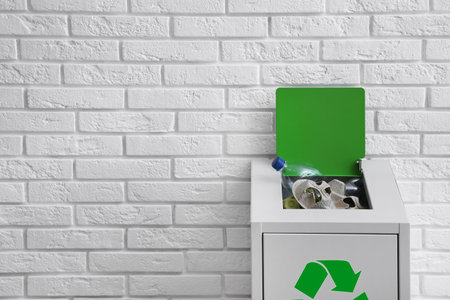 Overfilled trash bin with recycling symbol near brick wall. Space for textの写真素材