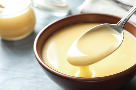 Spoon of pouring condensed milk over bowl on table, closeup with space for text. Dairy productsの写真素材