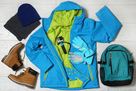 Set of warm clothes and action camera on wooden background, flat lay. winter holidays