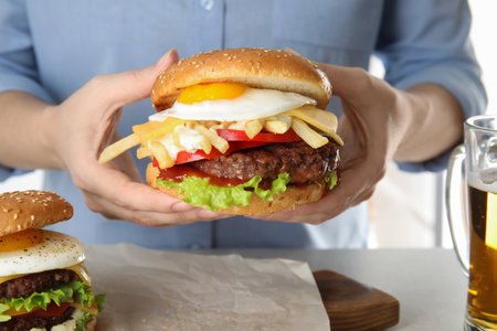 Woman holding tasty burger with fried egg over table, closeupの写真素材