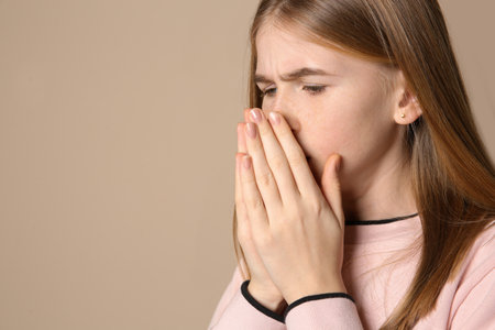 Teenage girl suffering from cough on color background. Space for textの写真素材