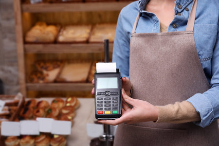 Woman holding payment terminal in bakery, closeup. Space for textの写真素材