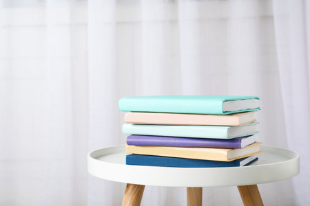 Stack of books on table against curtain. Space for text