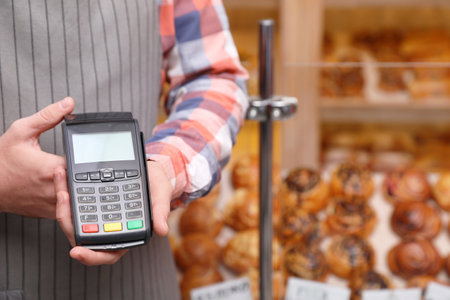Cashier holding payment terminal in bakery, closeup. Space for textの写真素材