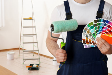 Male decorator with paint roller and color palette samples in empty room, closeup. Space for textの写真素材