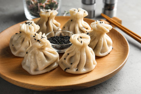 Wooden plate with tasty baozi dumplings and sesame seeds on tableの写真素材