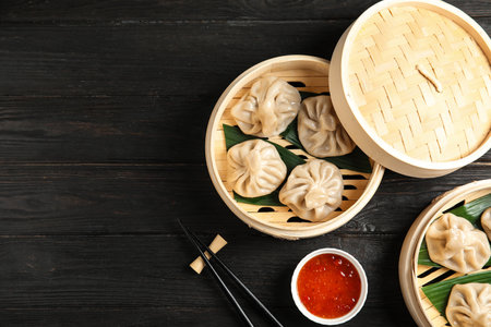 Bamboo steamers with tasty baozi dumplings, chopsticks and bowl of sauce on wooden background, top view. Space for textの写真素材