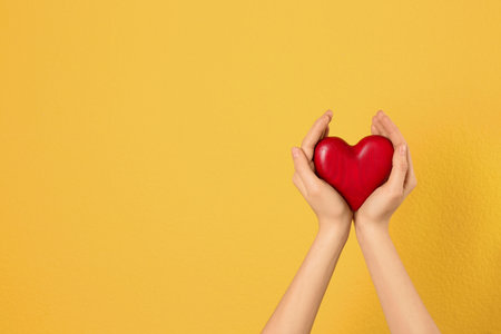 Woman holding decorative heart in hands on color background, space for textの写真素材